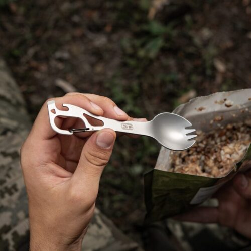 Spork M-Tac kasutusel toidu söömisel looduses, käes hoitav roostevabast terasest söögiriist karabiiniga.